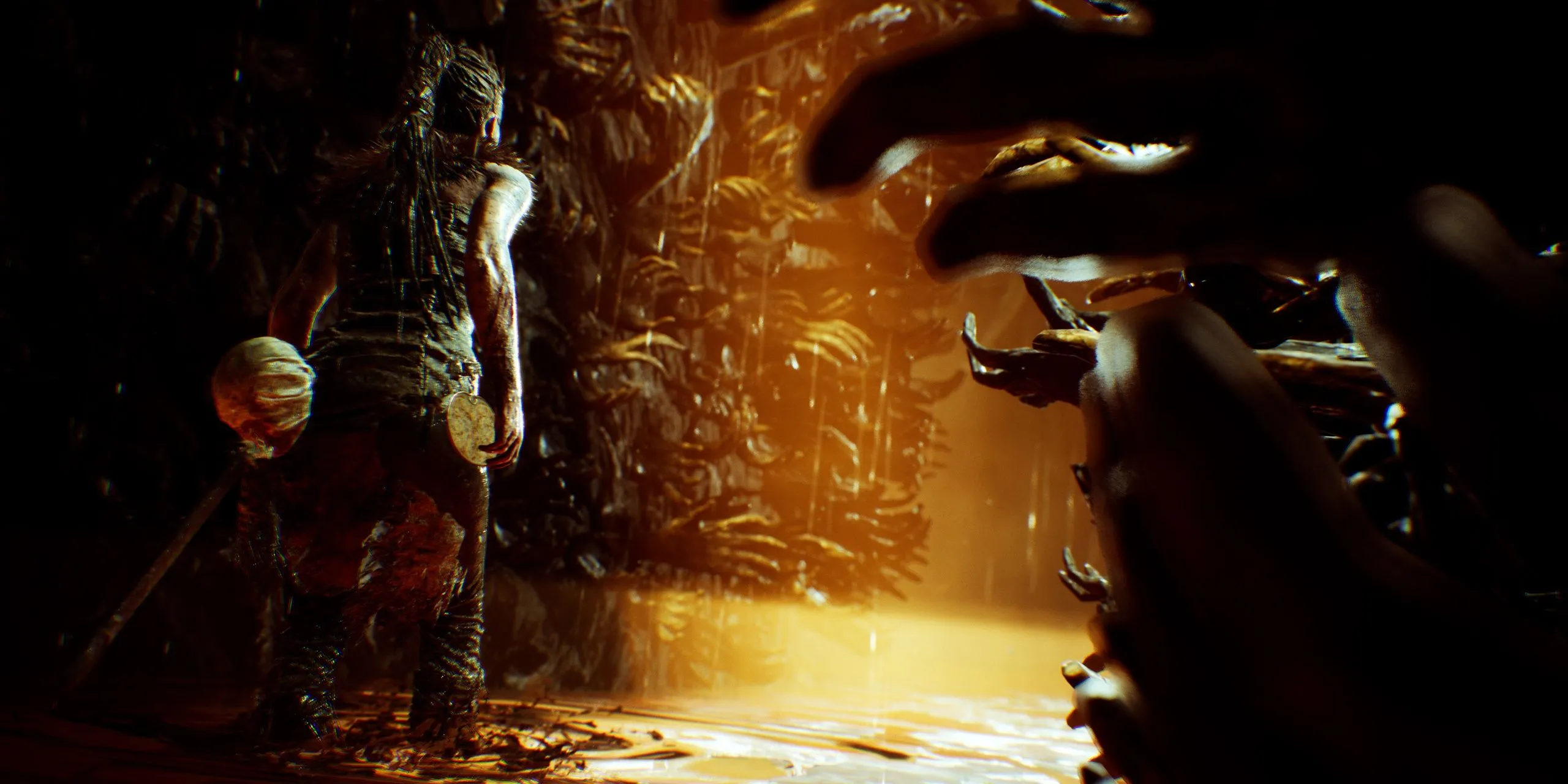 Senua đứng trước bức tường tay trong game Hellblade: Senua's Sacrifice, thể hiện trạng thái tâm lý phức tạp
